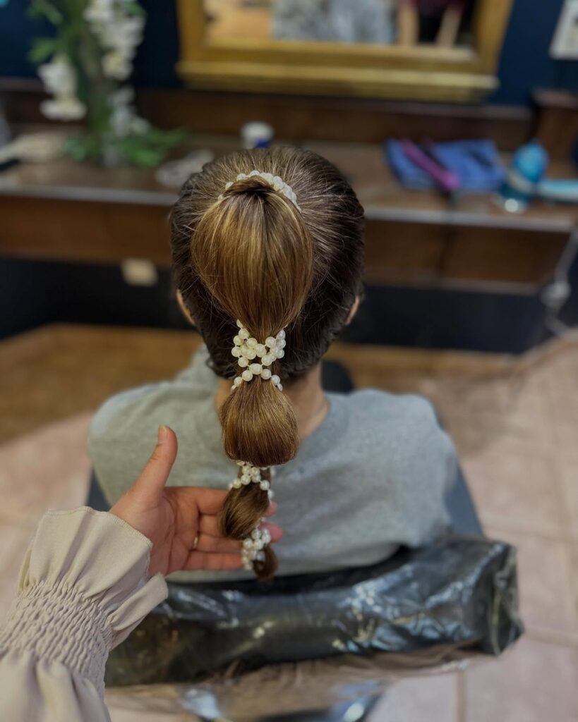 A woman seen from behind with her medium-length brown hair in a sleek bubble ponytail decorated with thick pearl hair accessories.