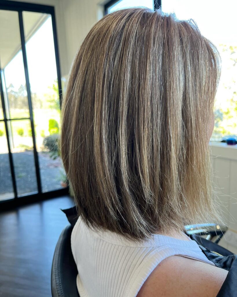 A side view of a woman with a straight, medium-length, ashy blonde lob featuring subtle layers and highlighted strands.