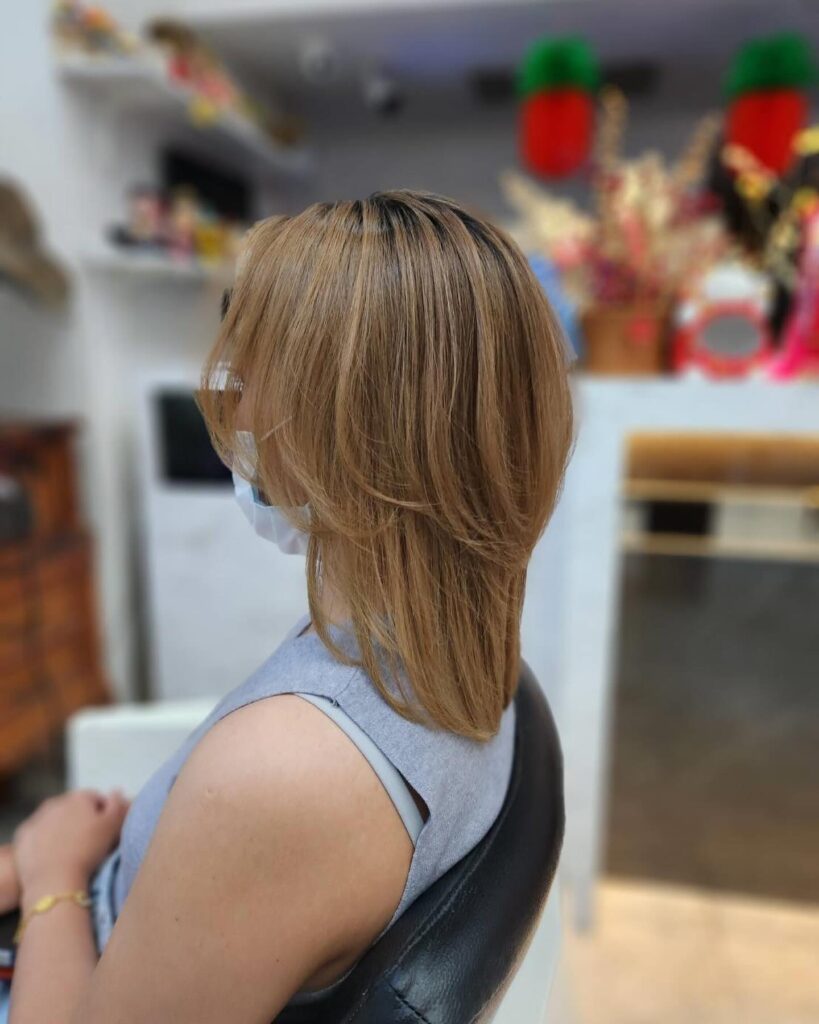 A side view of a woman with a straight medium-length warm blonde haircut featuring soft, curved layers and face-framing pieces.