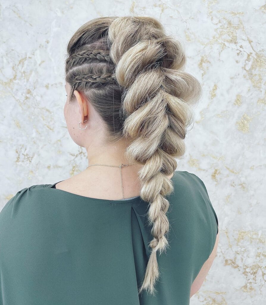 A woman from behind with ash-blonde hair styled in a large pull-through braid and detailed side cornrows.