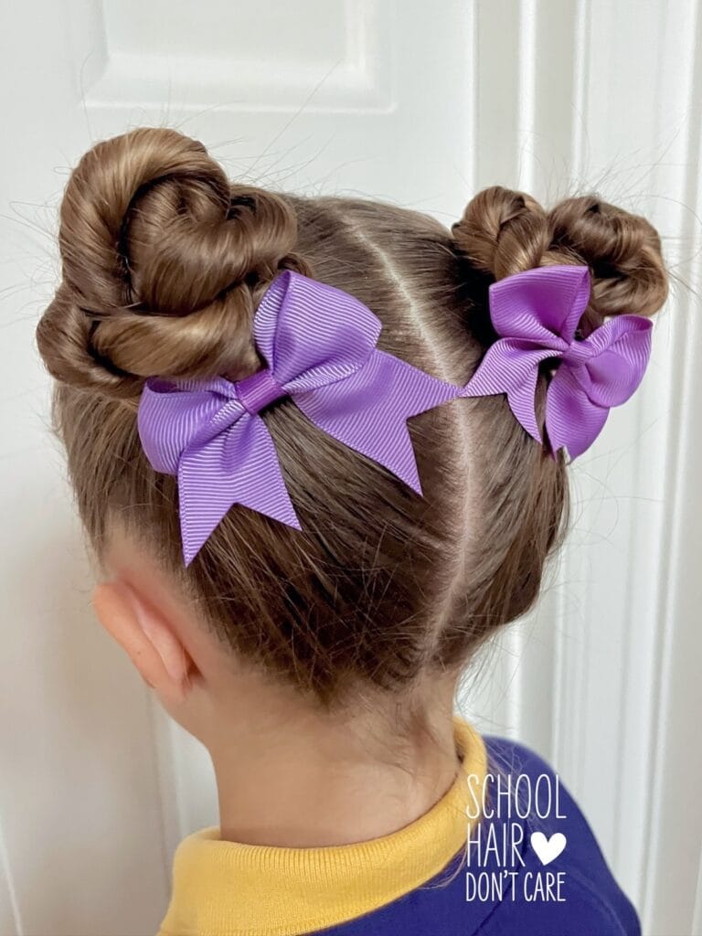 A young girl from behind with light brown hair styled in two braided space buns decorated with purple bows.