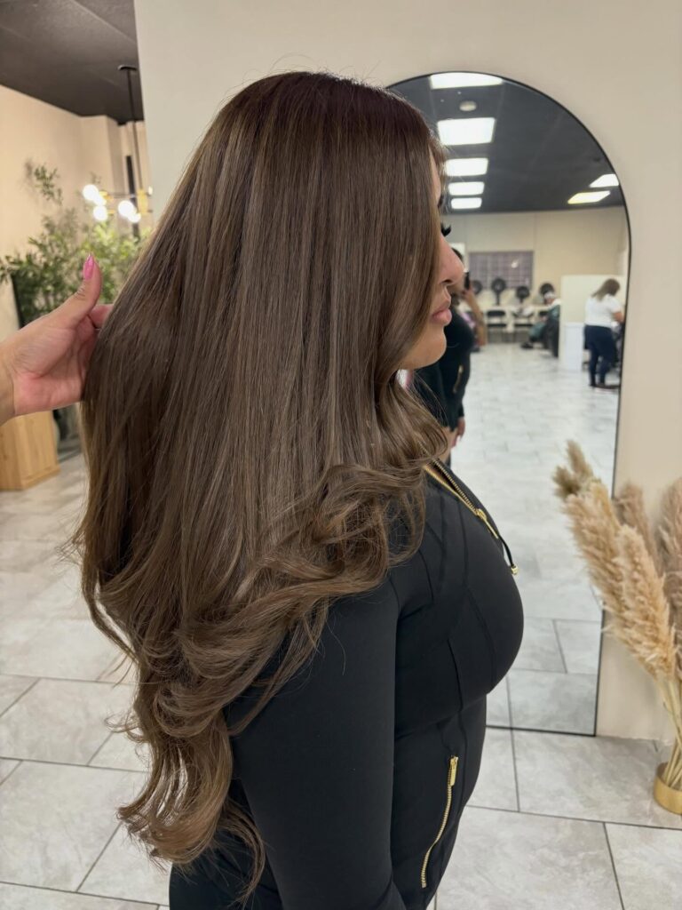 A woman with long mocha brunette hair featuring silky layers that are styled with a soft outward curl at the ends.