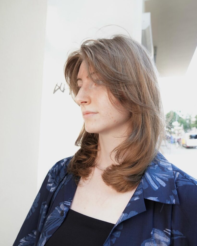 A woman with medium length warm brown hair featuring subtle internal layers and a relaxed wavy texture.