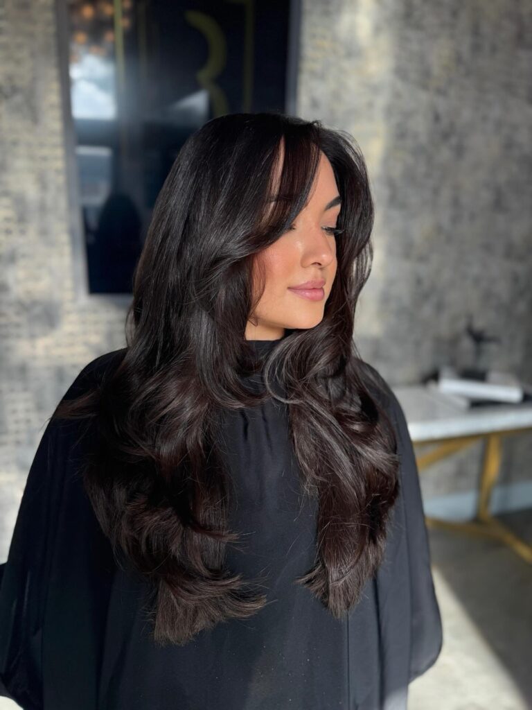 A woman with long dark chocolate brown hair styled with soft flowing layers and a gentle face framing fringe.