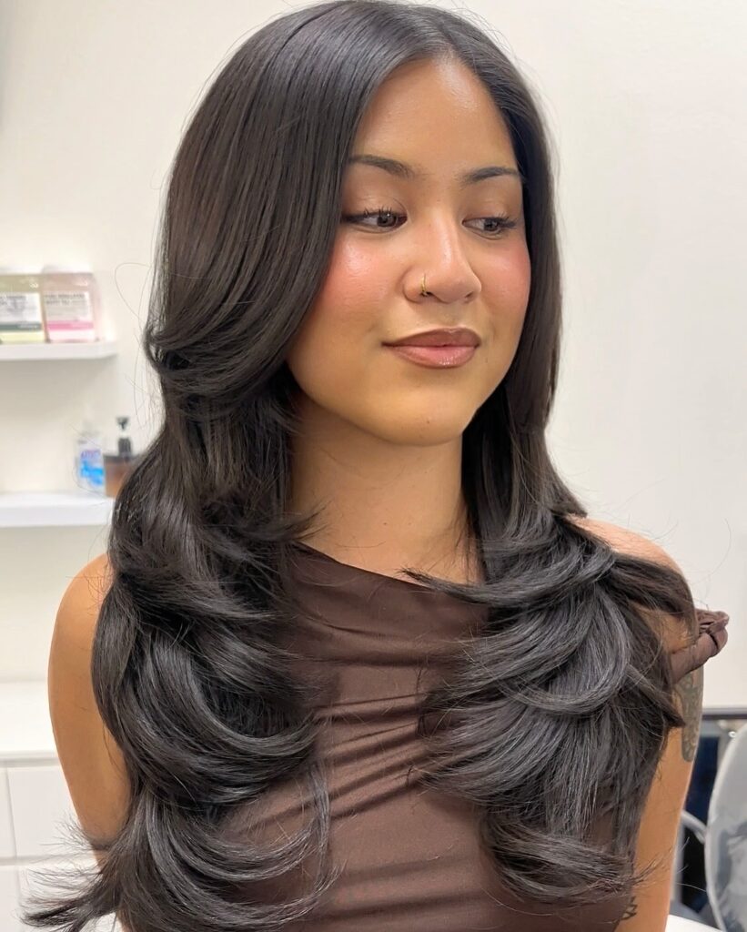 A woman with long dark espresso hair featuring dramatic butterfly layers and face framing bouncy curls.