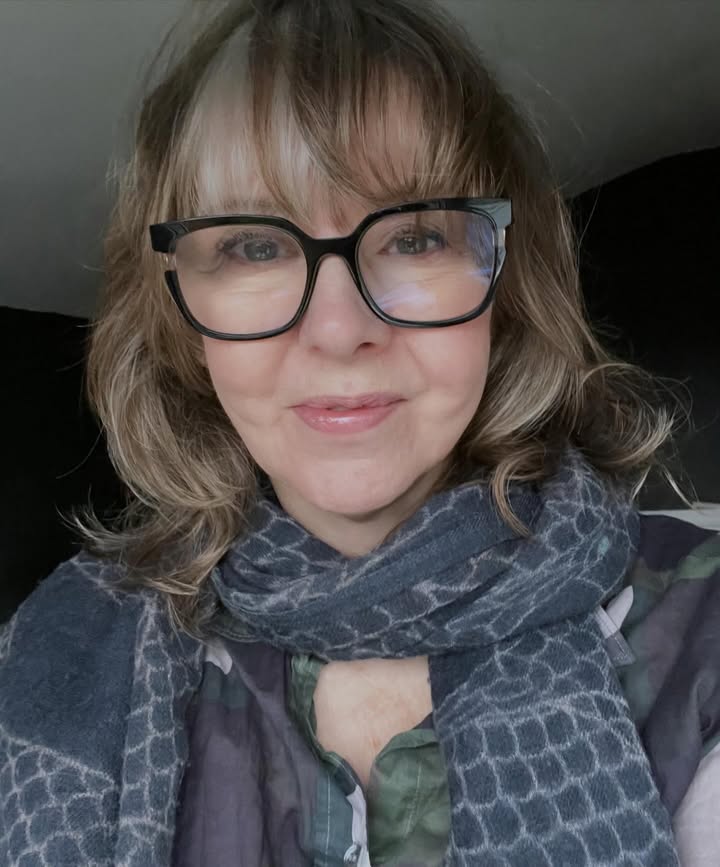 Wavy bob with wispy bangs styled lightly above glasses for a soft look.
