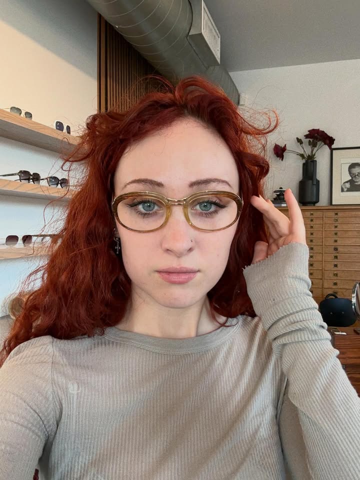 Wavy copper hair with light bangs styled comfortably above glasses.