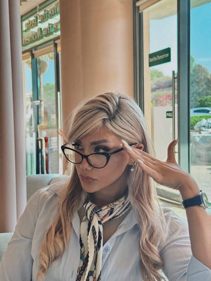 Long blonde layered hair with soft curtain bangs styled naturally with glasses.