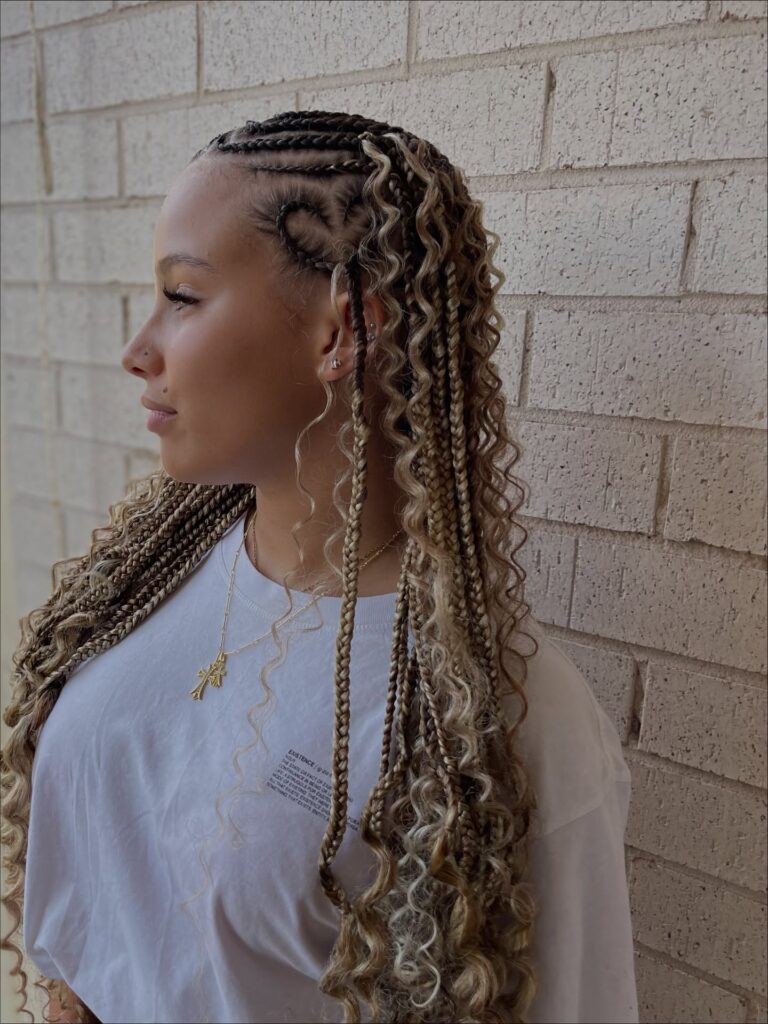 A woman in profile showing off blonde Fulani braids with a heart shaped cornrow design and loose curly bohemian strands.