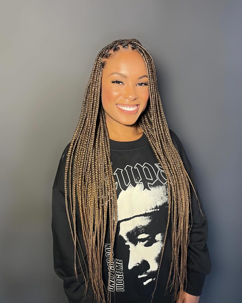 A woman smiling with long and thin sandy blonde Fulani braids that feature precise cornrows at the scalp.