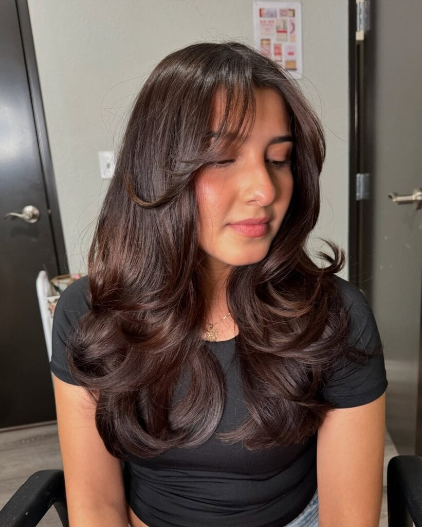 A woman with long dark brown hair styled in voluminous layers and large curled ends.