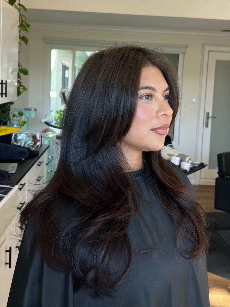 A woman with long dark brown hair styled in voluminous bouncy layers and a sweeping side fringe.