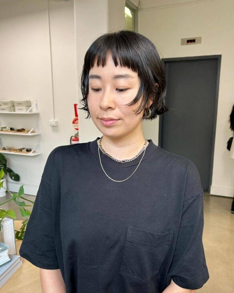 A woman with a short black bob hairstyle featuring piecey layers and a micro fringe.