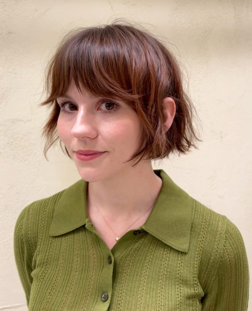 A woman with a textured auburn bob featuring wispy bangs and a soft tousled finish.