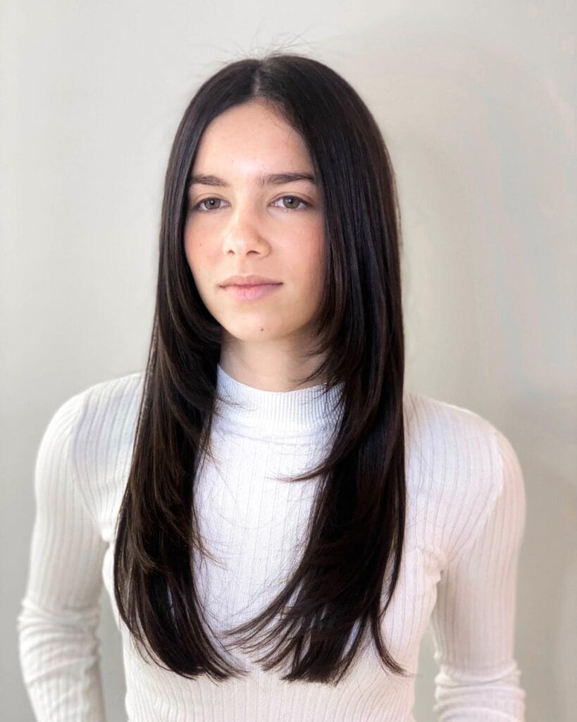 A woman with long dark brown hair styled in sleek face framing layers and curtain bangs.