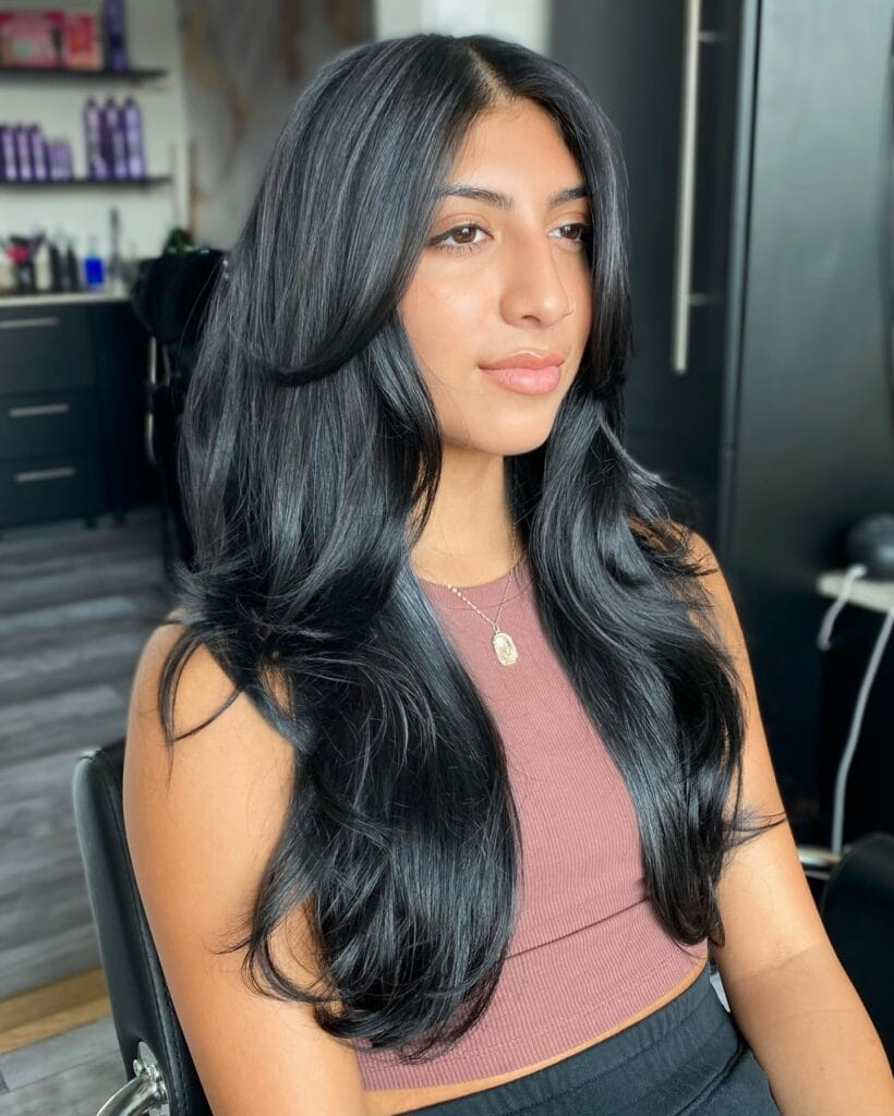 A woman with long jet black hair featuring voluminous blowout layers and curled ends.