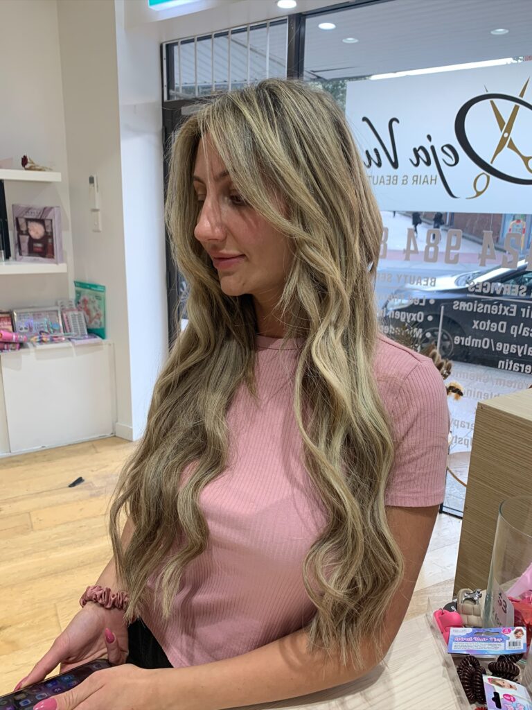 A woman with sleek blonde hair tied into a polished low ponytail with elegant soft waves.