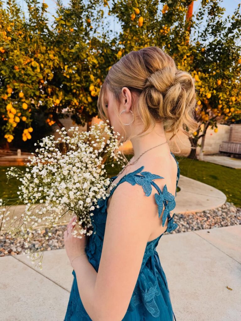 A woman with honey blonde hair styled in a loose twisted low updo with soft face-framing curls.