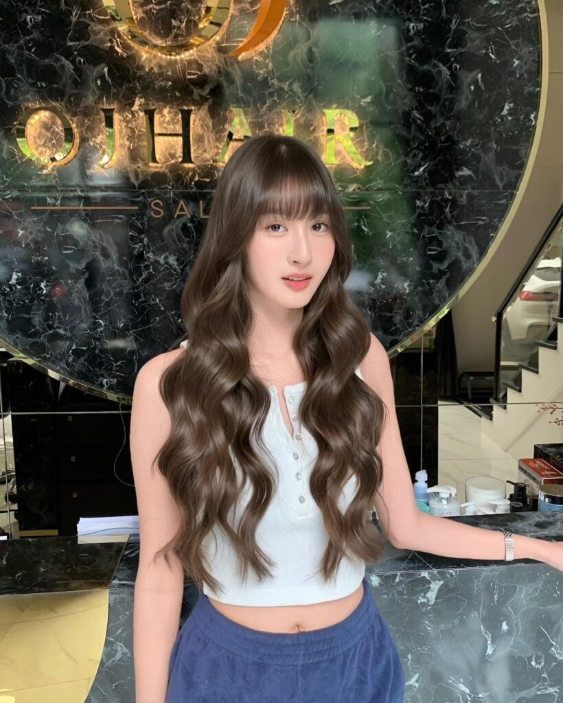 A woman with long glossy espresso brunette hair featuring wispy bangs and perfectly defined mermaid waves.