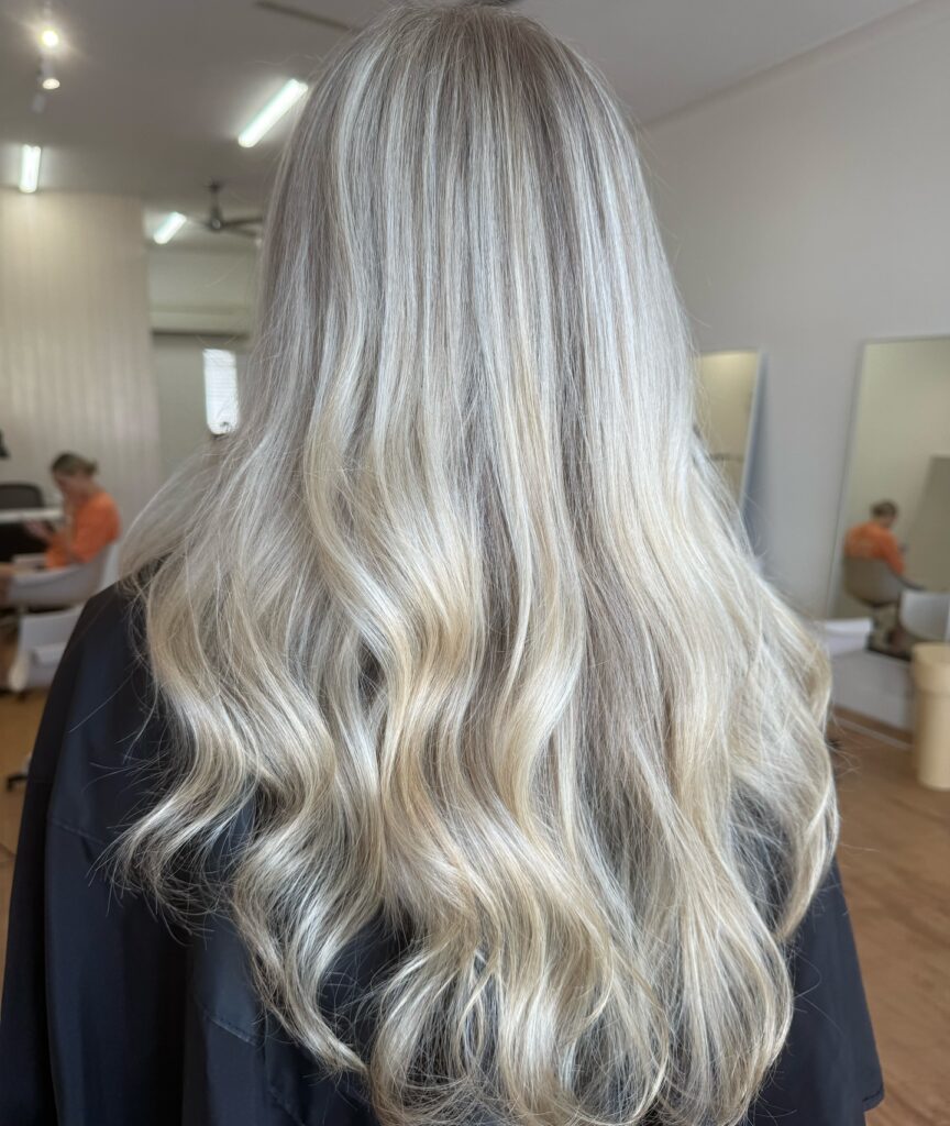 A woman with long silky champagne blonde hair styled in loose beachy waves cascading down her back.