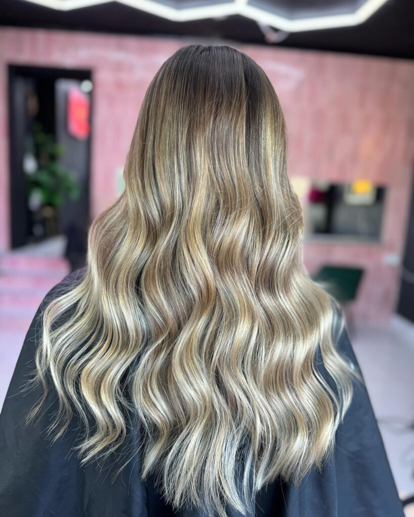 A woman shows off long ash blonde hair styled in soft ribbon waves with a dimensional balayage.