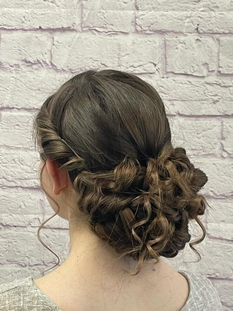 A woman with brunette hair styled in a low chignon made of pinned curls and side twists.