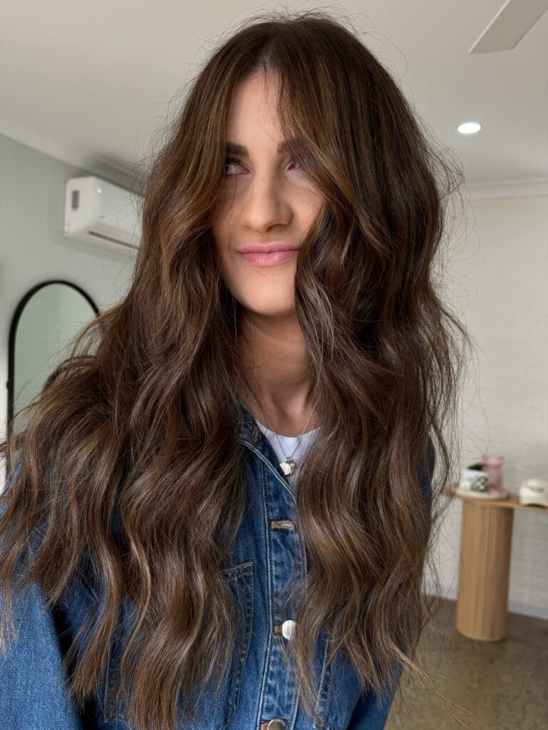 Long wavy brunette hair with curtain bangs and voluminous beachy texture.