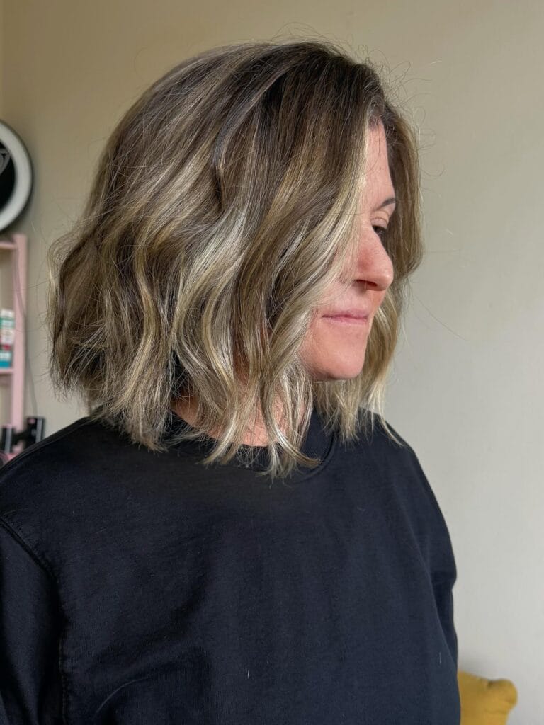 Shoulder-length blonde wavy lob with dark roots and soft waves.