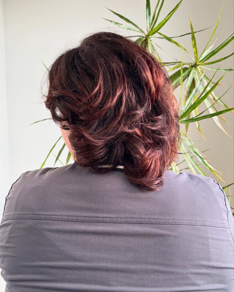 A medium layered tomboy haircut with soft flowing layers, flipped ends, and warm auburn tones.