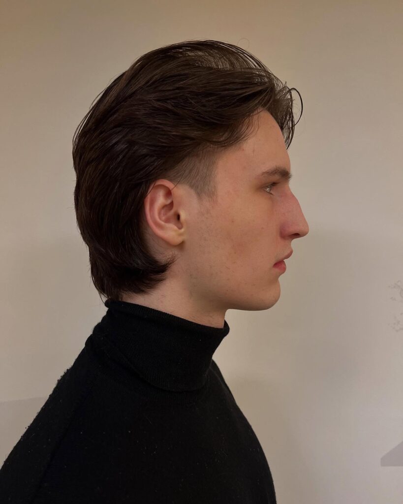 A sleek layered tomboy haircut with tapered sides, longer top layers, and smooth dark brown hair styled back.