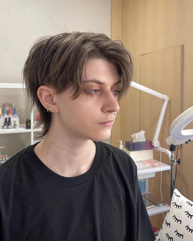 A layered tomboy haircut with a soft mullet shape, longer back layers, and ash brown tones with natural movement.