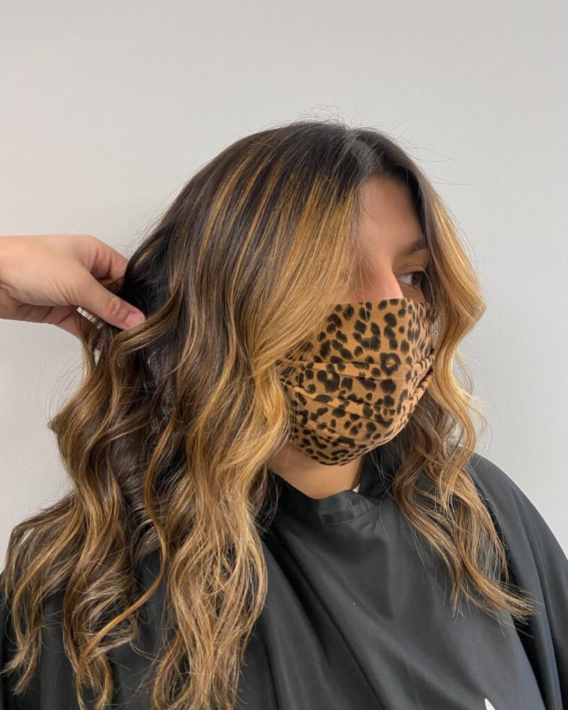 A woman with long layered blonde balayage hair styled in soft beachy waves.
