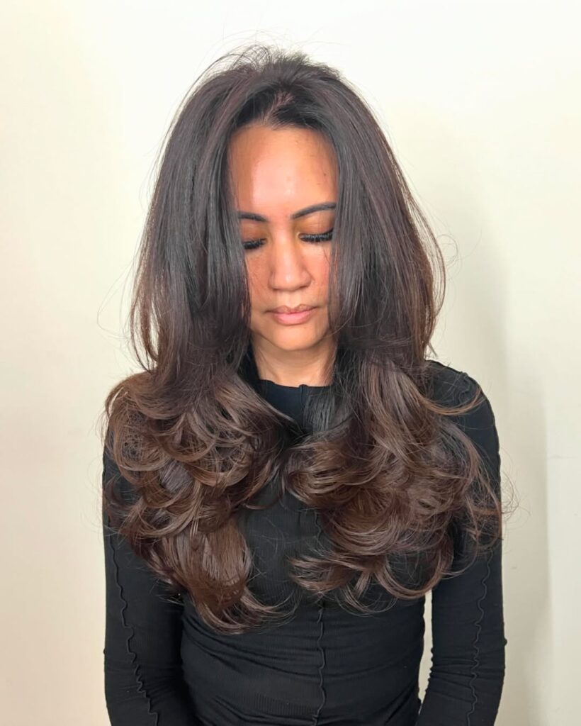 A woman with long layered hair styled in soft rounded waves with natural volume.