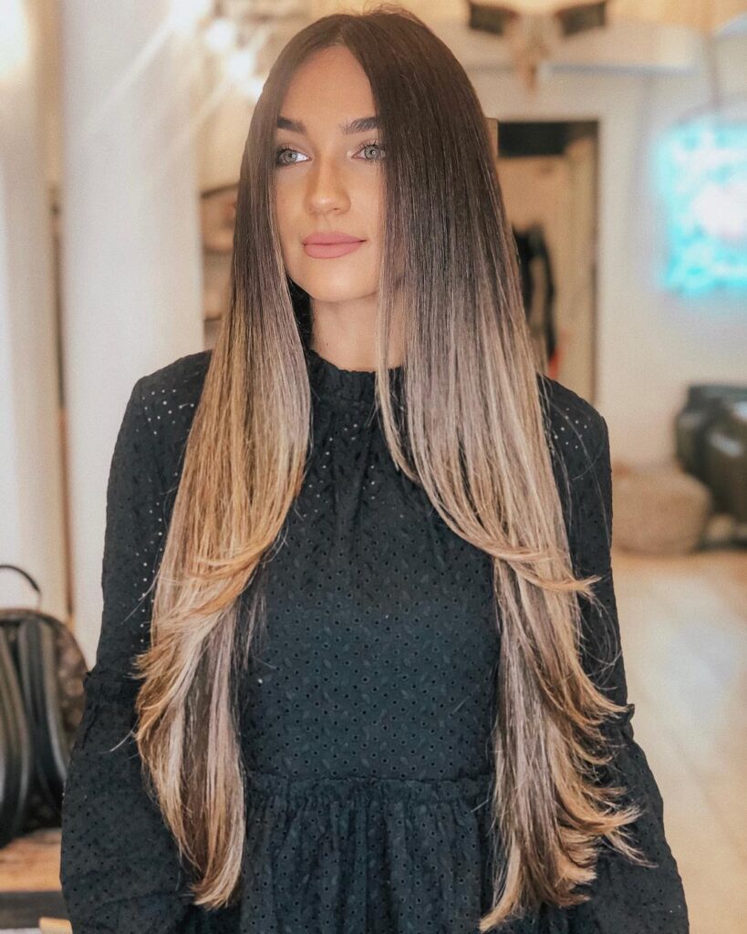 A woman with extra long layered hair featuring soft waves and lightened ends.