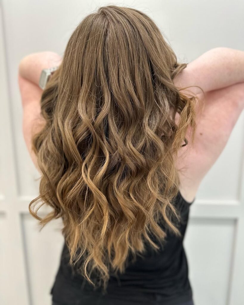 A woman with long layered brown hair styled in soft natural waves.