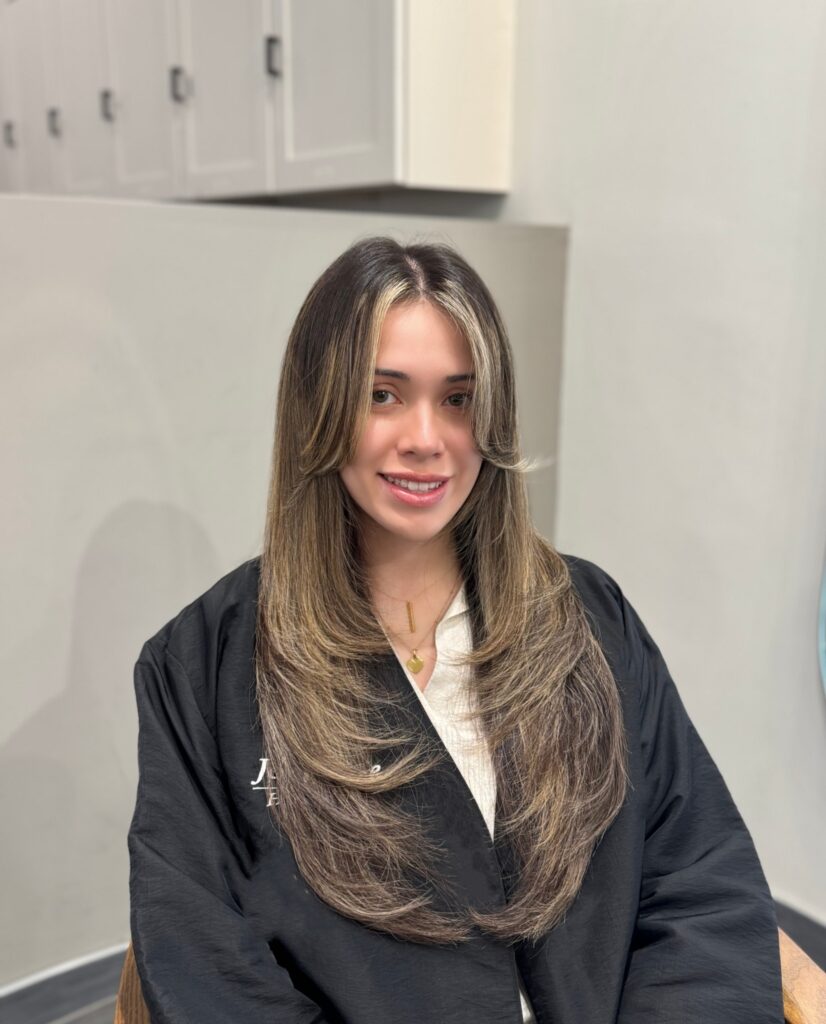 A woman with very long dark hair featuring bright blonde face framing highlights and dramatic tiered layers.