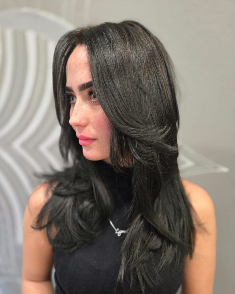 A woman with medium length jet black hair featuring sharp tiered layers and a middle part.