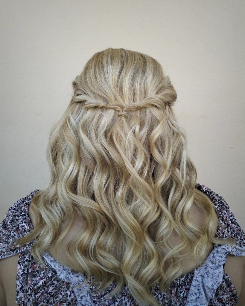 Long blonde wavy hair styled in a soft half up hairstyle with loose curls flowing down the back.