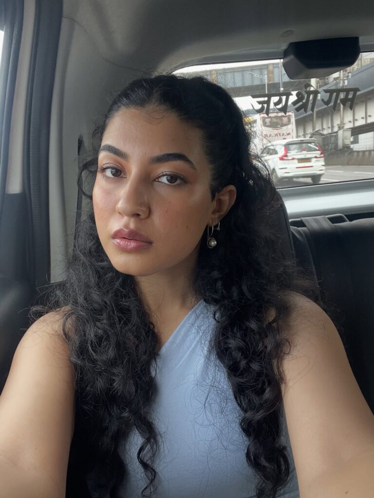 A woman with long curly hair styled half up with defined curls and face framing pieces.