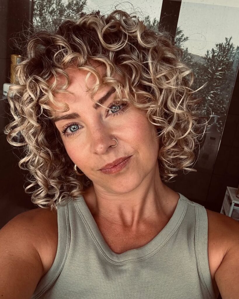 Short blonde curly bob with defined tight curls and voluminous shape framing the face.