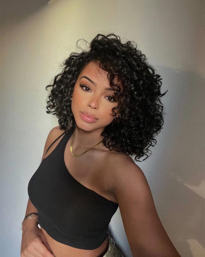 Short dark curly bob with defined curls styled with side volume and a soft shape around the face.