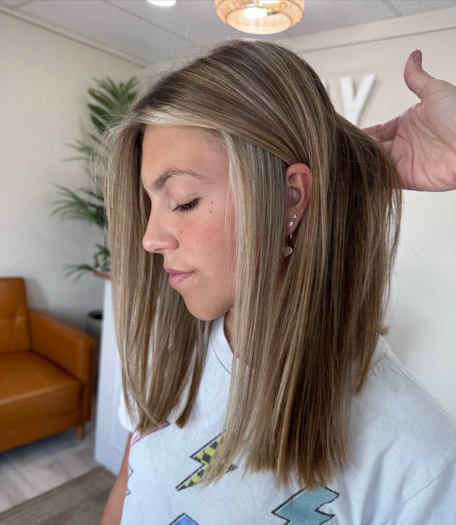 A side profile of a woman with a sleek, straight medium length lob featuring a bright bronde balayage and a striking money piece.
