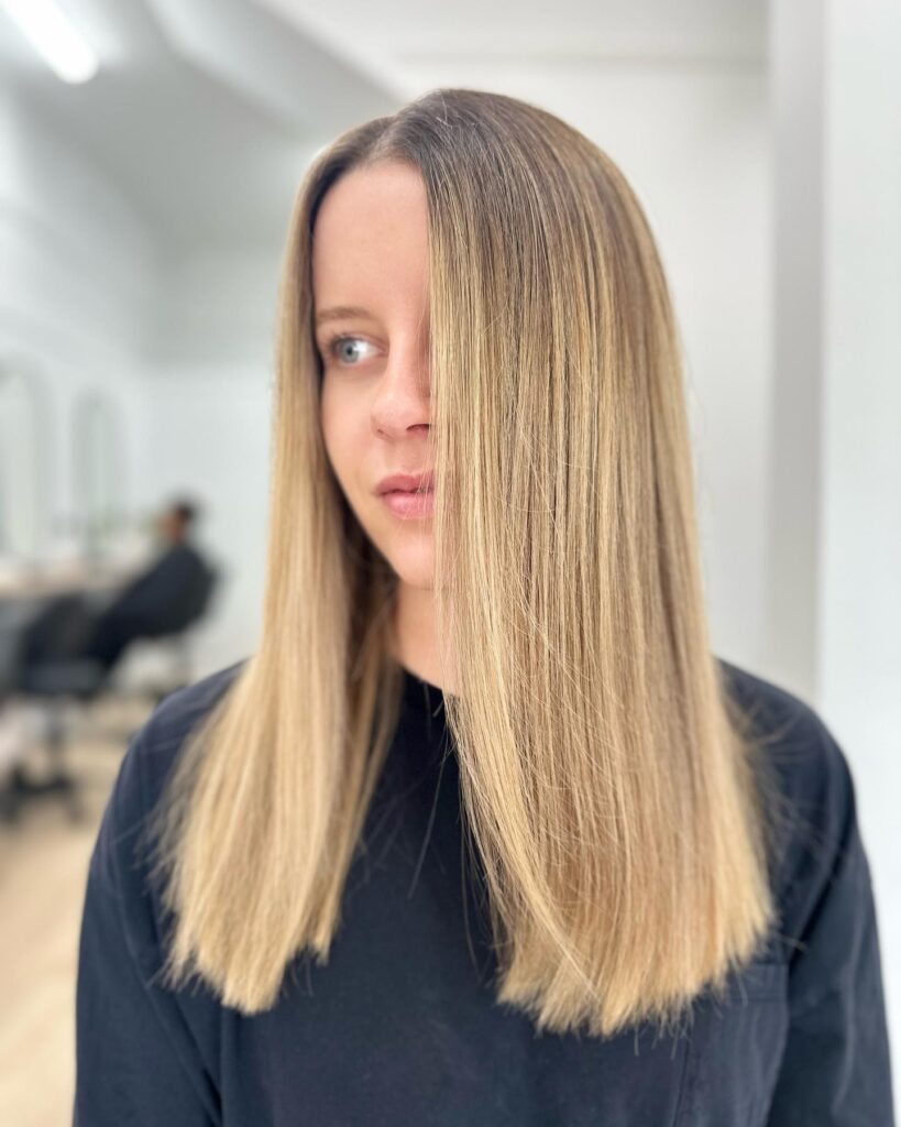 A woman with straight sandy blonde hair cut in a sharp blunt style at medium length.