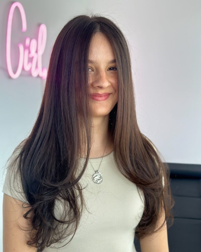 A smiling woman with very long dark brown hair featuring smooth butterfly layers flicked at the ends.