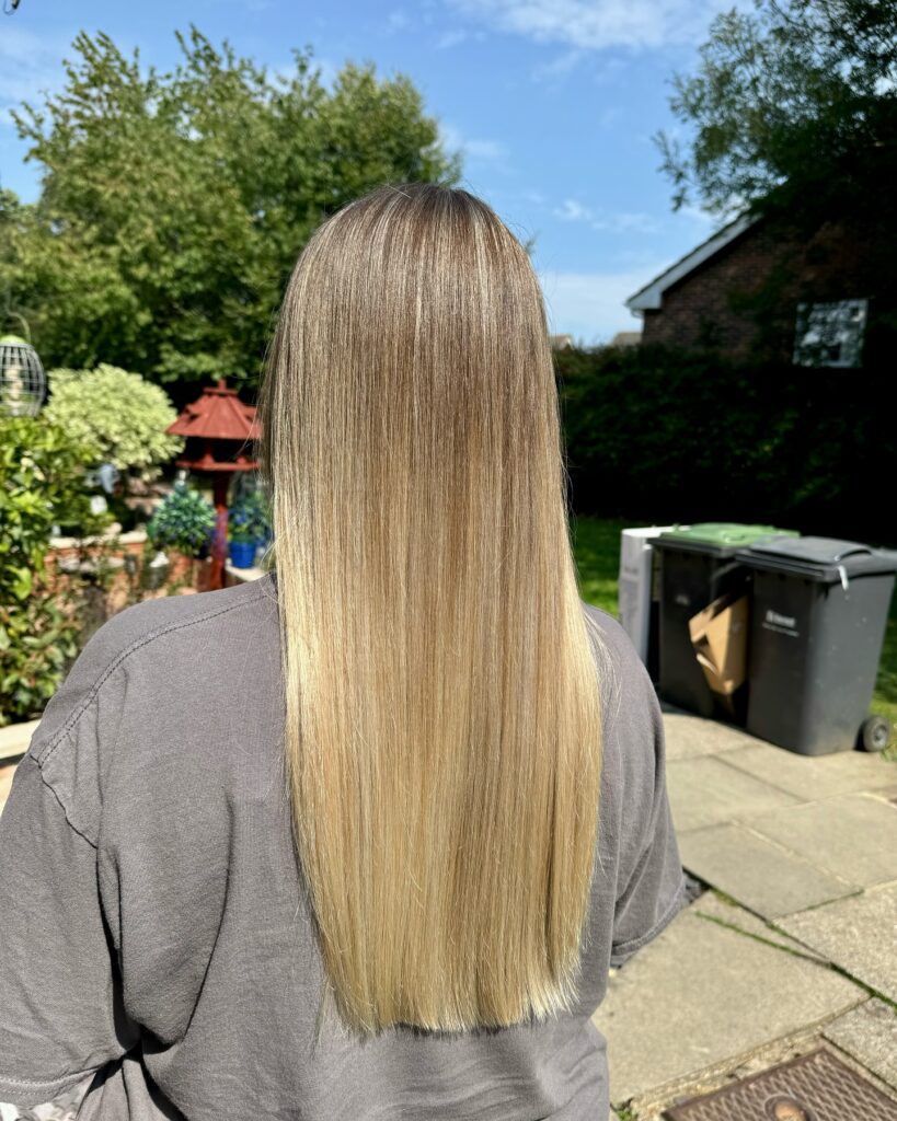 The back view of a woman with long straight hair featuring a smooth blonde balayage and blunt ends.