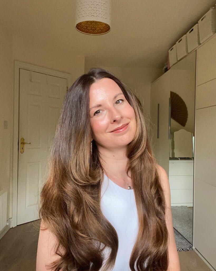 A woman with long thick brunette hair featuring face framing layers and soft curled ends.