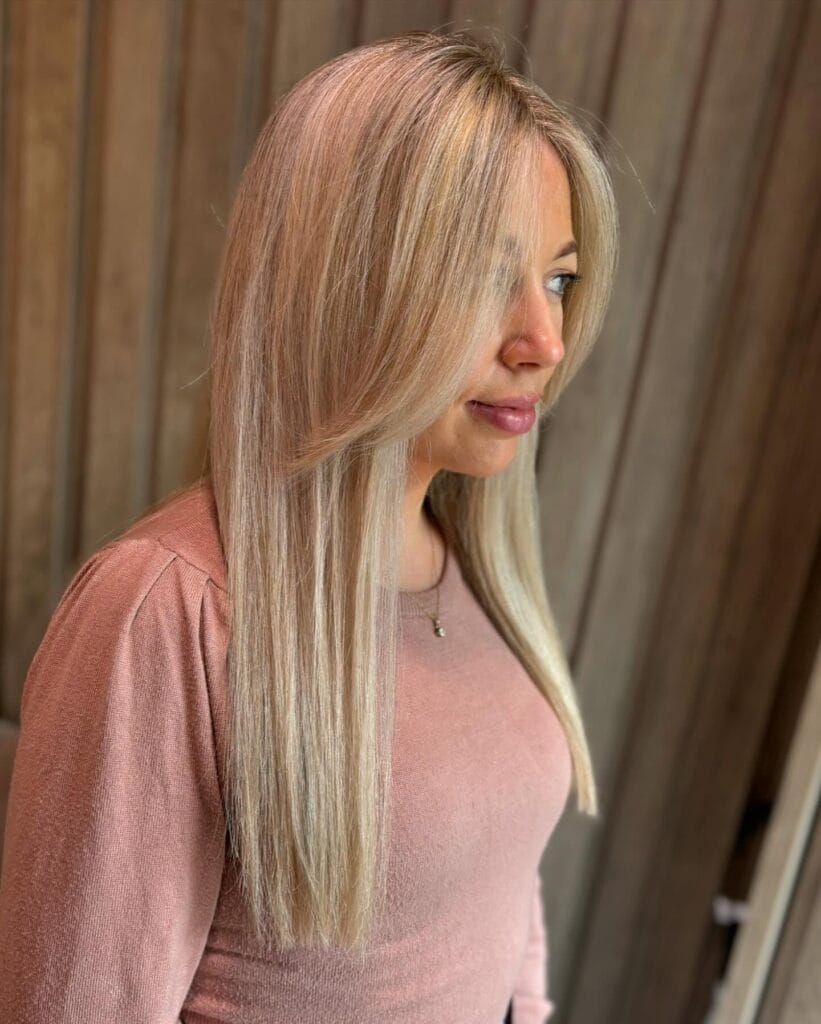 A woman with long straight ash blonde hair featuring sharp face framing layers and a center part.