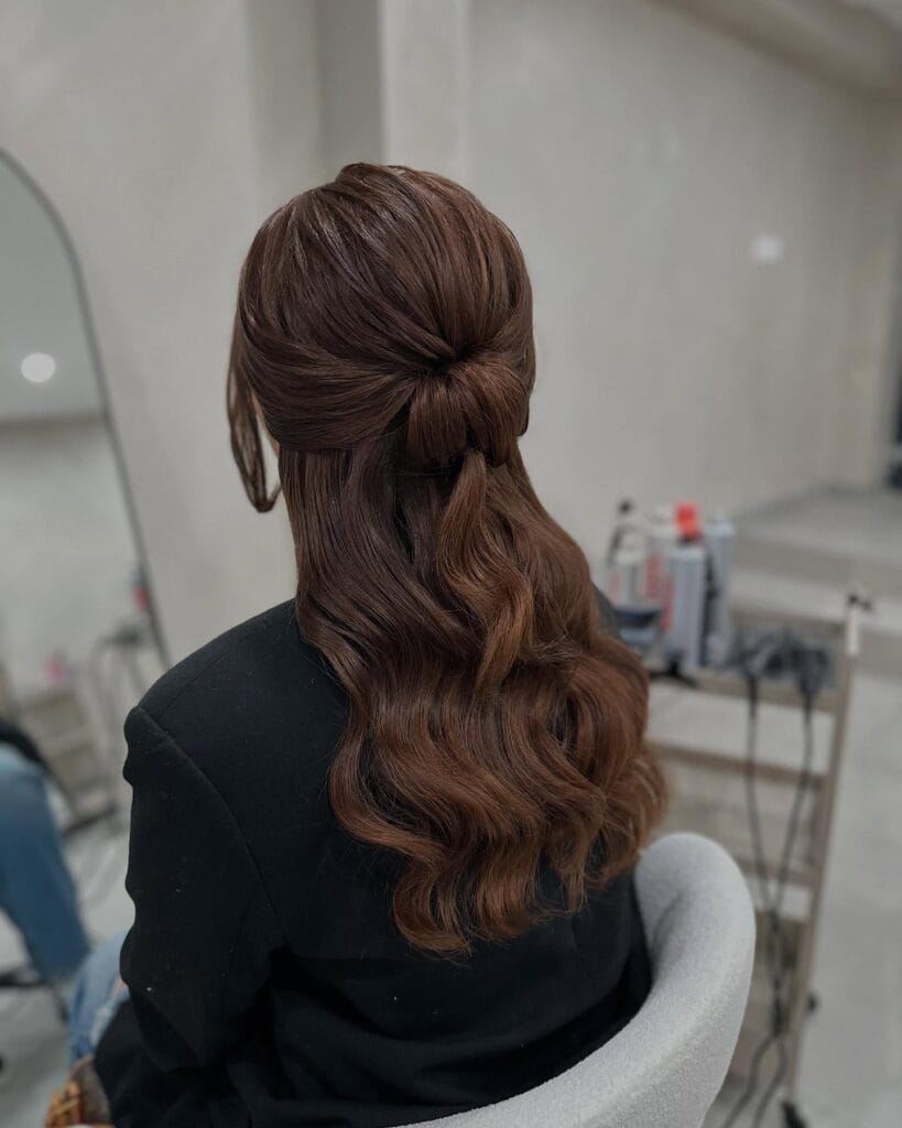 A back view of a woman with wavy brunette hair in a half up tucked twist hairstyle.