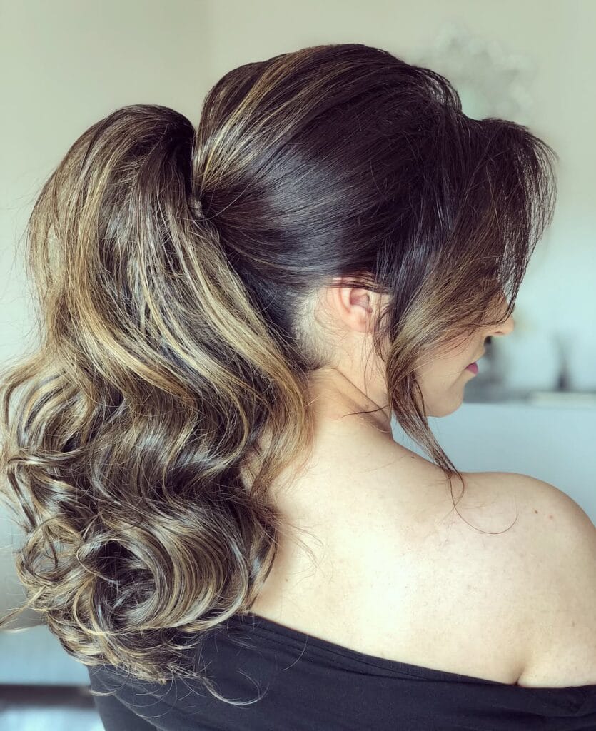 A woman from the side showing a high ponytail with thick wavy brunette hair and blonde highlights.