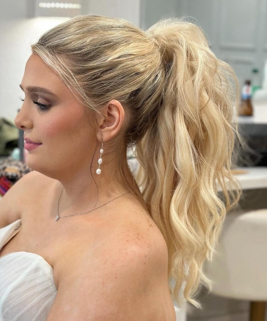 A side view of a woman with long wavy blonde hair styled in a high voluminous ponytail.